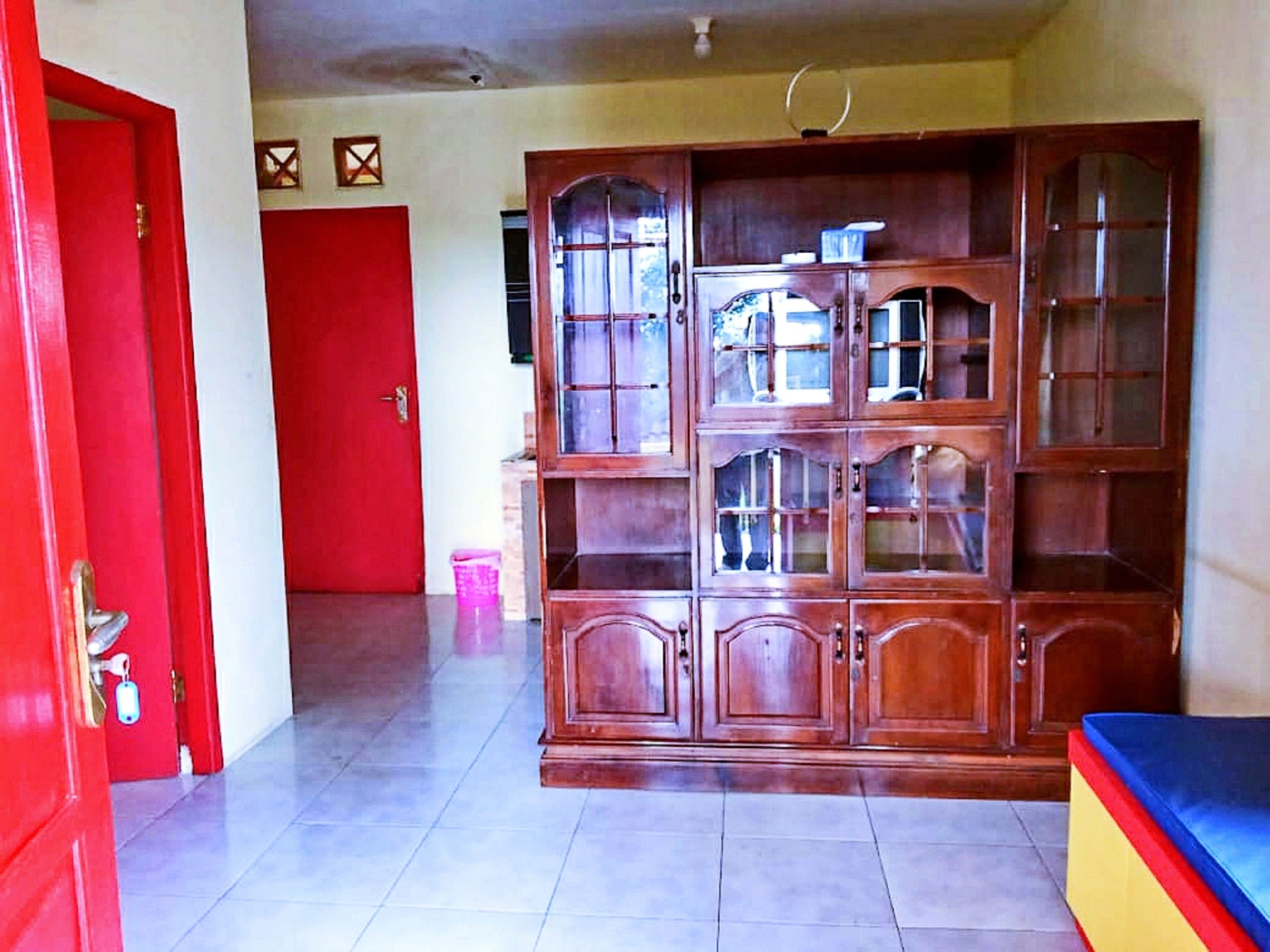 A room with a large wooden cabinet, a red door, and a tiled floor.