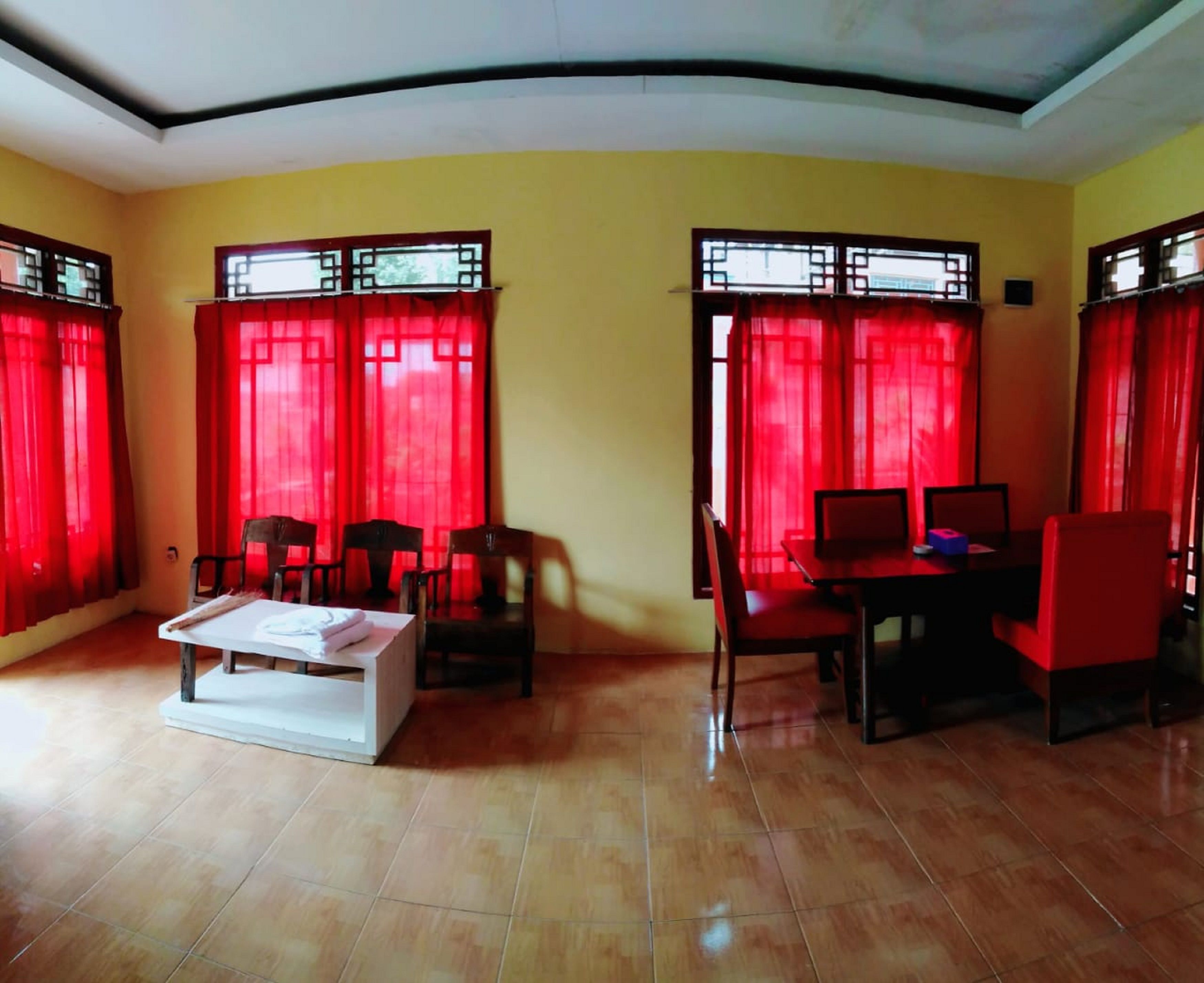 A room with yellow walls, red curtains, a white sofa, and a dining table with chairs.