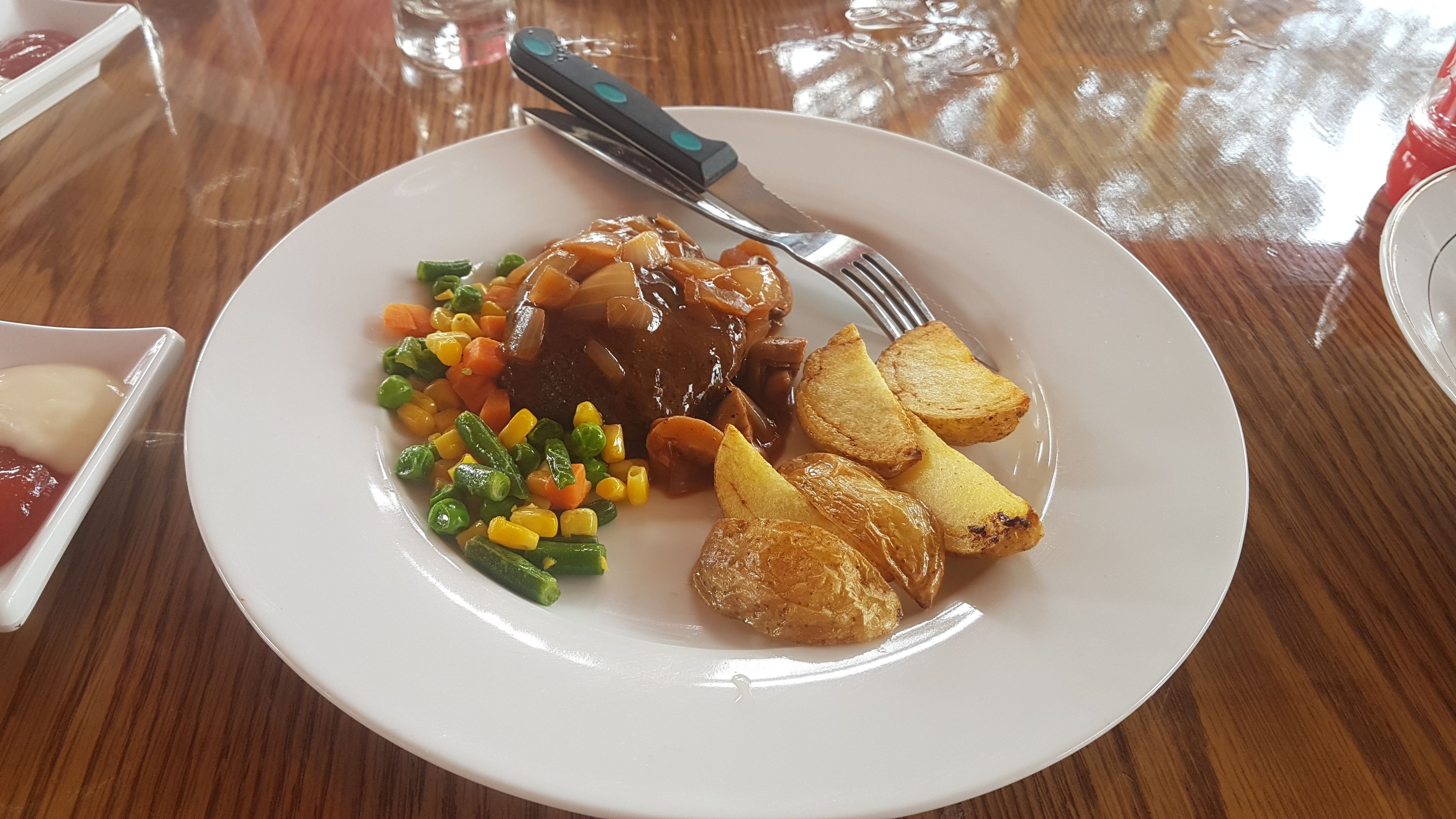Un plato de comida con un filete, verduras y patatas asadas sobre una mesa de madera.