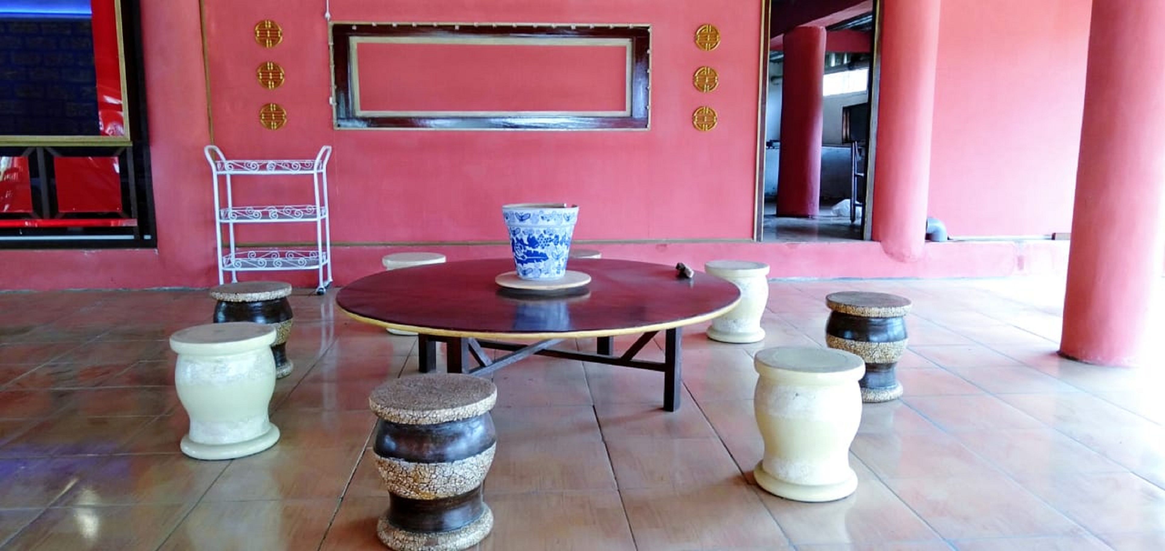 Une table ronde, sur laquelle est posé un vase bleu au centre, est entourée de six tabourets.