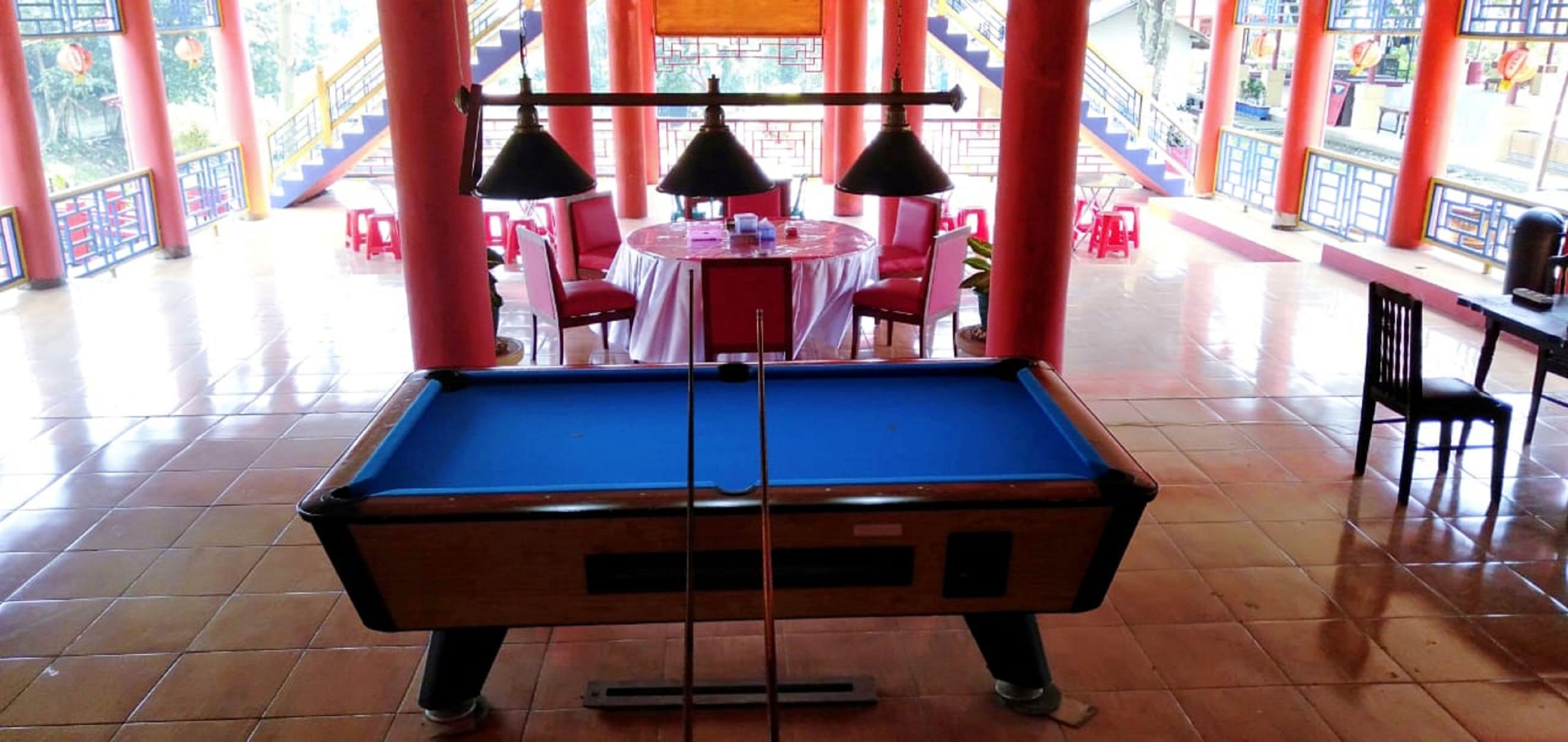 A pool table in a brightly lit room with red pillars and a tiled floor.