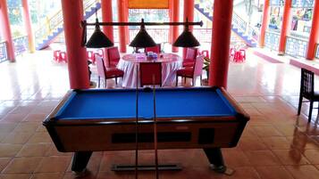 A pool table in a brightly lit room with red pillars and a tiled floor.