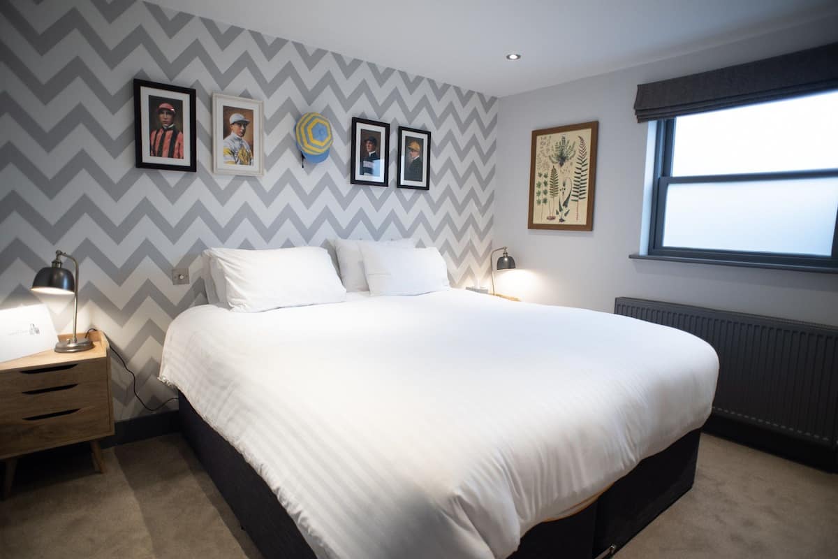 A bedroom with a large bed, a nightstand with a lamp, a dresser, and a window with a view.