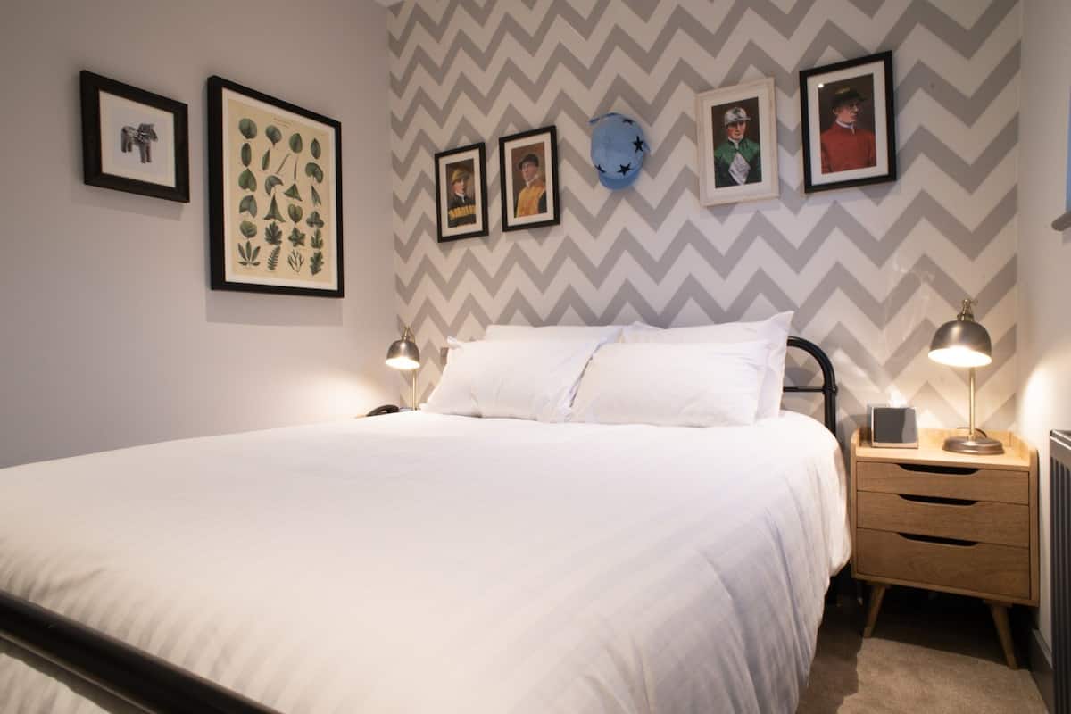 A neatly made bed with white linens, a wooden nightstand with a lamp, and a wall with a chevron pattern.