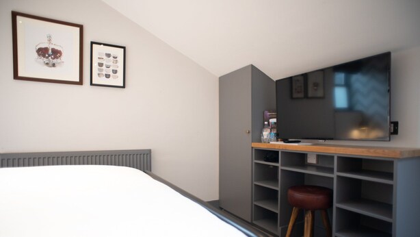 A bedroom with a bed, a desk with a computer, a chair, and a TV. - The Albert Arms (Esher)