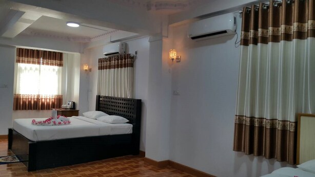 A hotel room with a bed, a nightstand, an air conditioning unit, and a window with curtains. - Golden Palace Hotel Hpa An (Hpa-An)