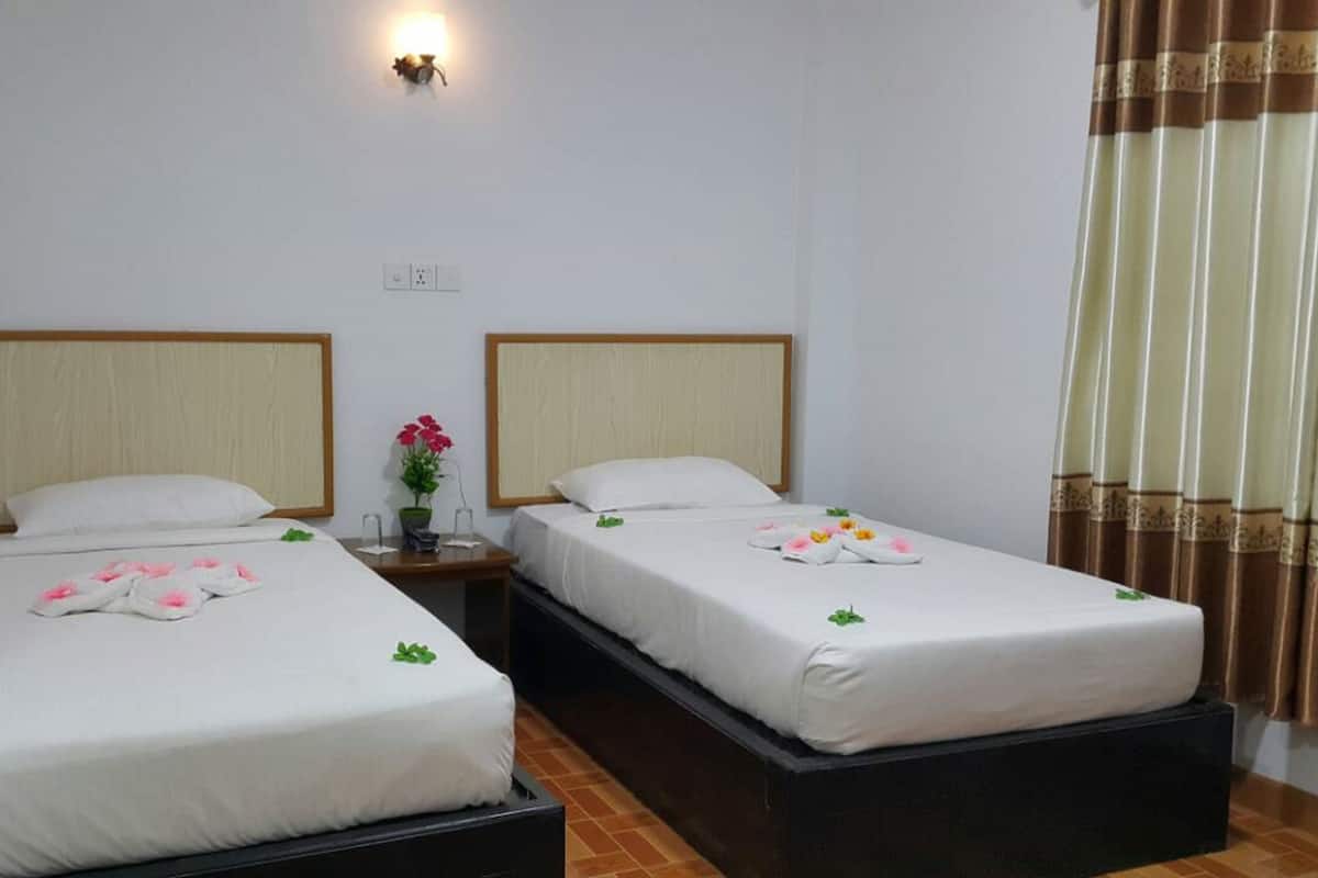 Una habitación de hotel con dos camas individuales, una mesita de noche con un florero y una lámpara fijada a la pared.