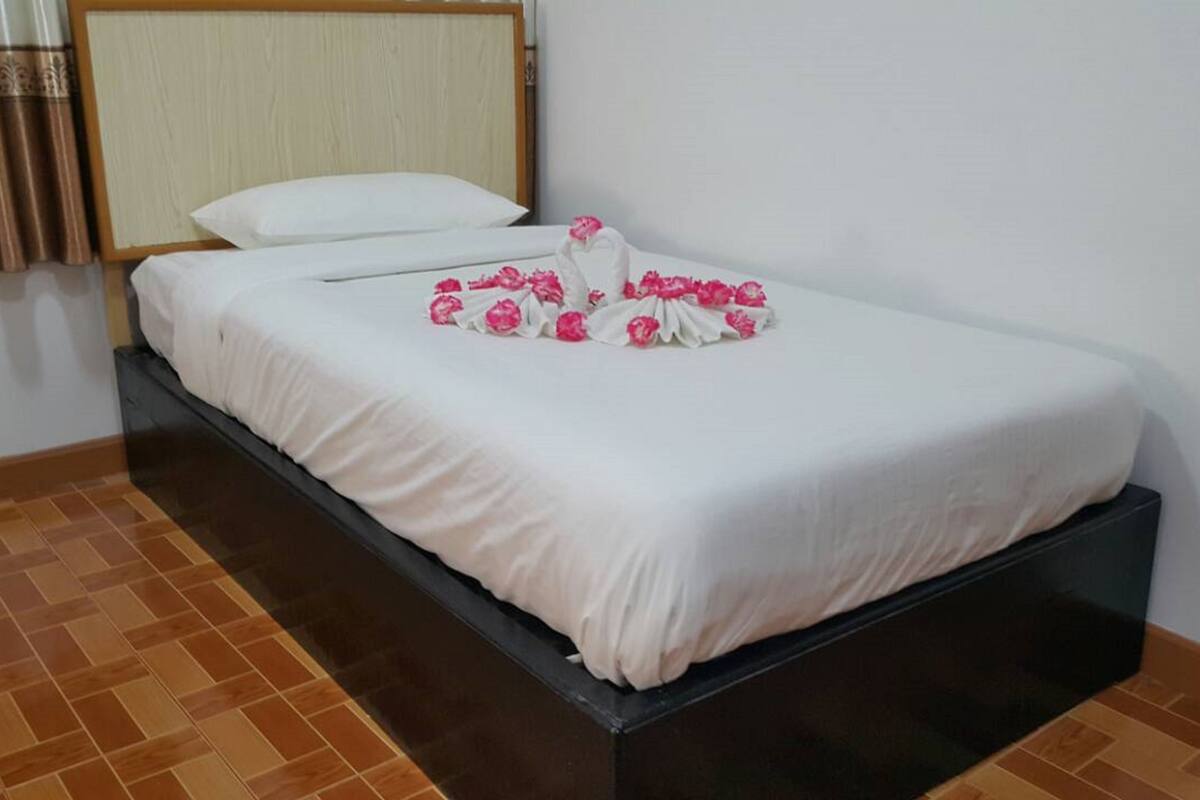 Una cama individual con un edredón blanco y flores rosadas dispuestas en forma de corazón.