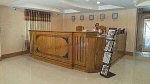 A reception desk with a wooden finish, a bulletin board with printed materials, and a clock on the wall. - Golden Palace Hotel Hpa An (Hpa-An)