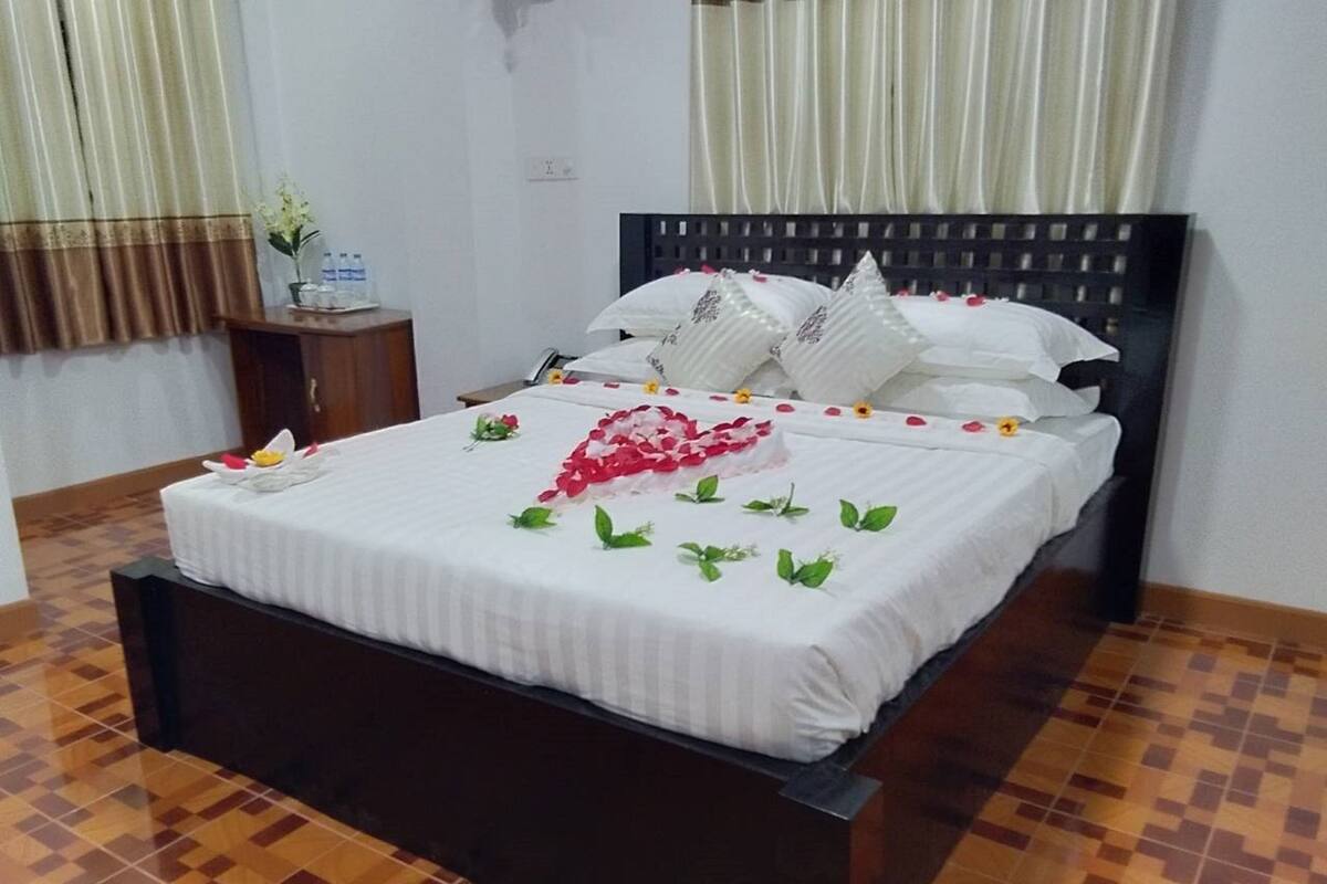 Una cama bien hecha con sábanas blancas y flores decorativas, un cabecero de madera oscura y un suelo de baldosas.