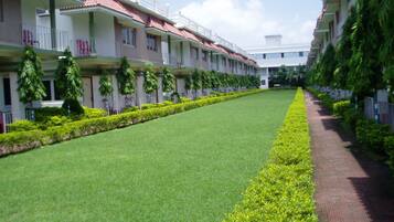 A hotel with a long, straight pathway flanked by neatly trimmed hedges and a row of balconies with red-tiled roofs.