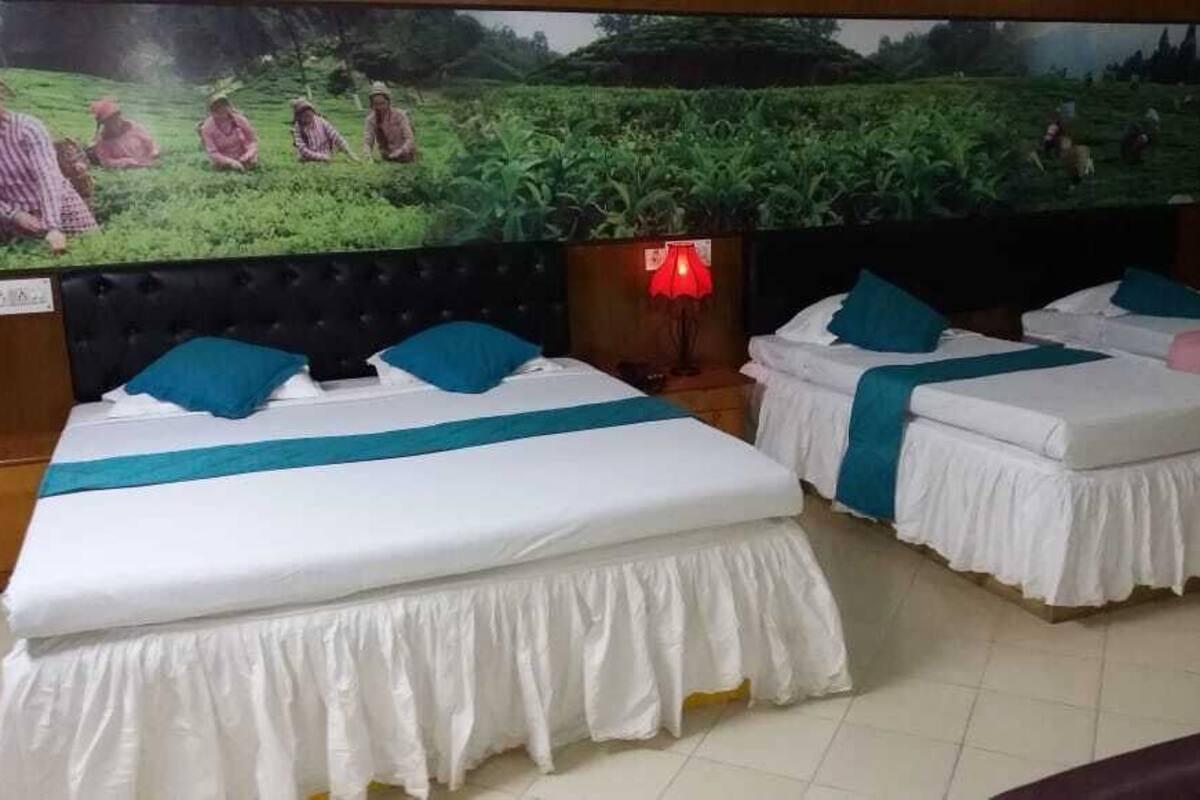 Une chambre d’hôtel avec deux lits, chacun agrémenté de draps blancs et de touches de couleur turquoise, une grande peinture représentant un paysage rural et une lampe rouge posée sur une table de chevet en bois.
