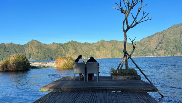A wooden dock extending into a body of water with two people seated at a table. - N'jung Bali Camp (Kintamani)