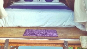 A cozy, triangular room with a bed, white curtains, and a wooden ceiling. - N'jung Bali Camp (Kintamani)