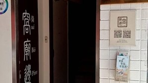 A hallway with a door labeled in Chinese characters, a tiled wall with a small poster, and a hanging light fixture. - Temple Side - Hostel (Tainan)