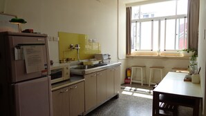 A compact kitchen with a refrigerator, microwave, sink, and a window providing natural light. - Temple Side - Hostel (Tainan)
