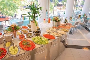 Uma mesa de buffet com diversos tipos de comida e um vaso de planta.