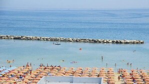 Une plage avec de nombreux parasols, où l’on peut voir des gens nager et prendre des bains de soleil.
