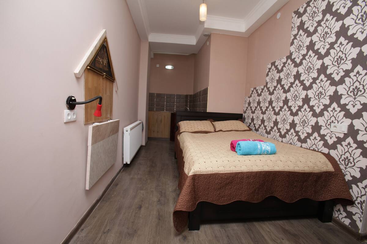 A bedroom with a bed, a radiator, a wall-mounted light, and a patterned wallpaper.