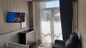 A living room with a flat-screen TV mounted on the wall, a black sofa, a white dresser, and a sliding glass door with curtains. - Mia B&B Tbilisi (Tbilisi)