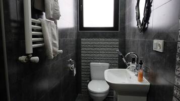 A bathroom with a white toilet, a sink with a soap dispenser, and a towel rack with towels.