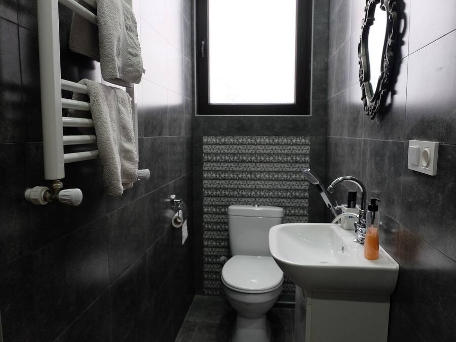 A bathroom with a white toilet, a sink with a soap dispenser, and a towel rack with towels.