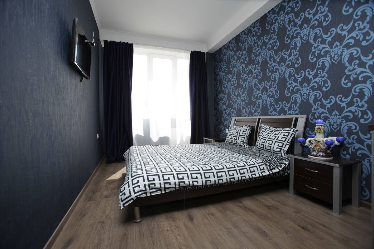 A bedroom with a bed, a nightstand, a TV, and a window with curtains.
