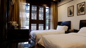 A hotel room with two beds, a desk, and a window with decorative lattice.