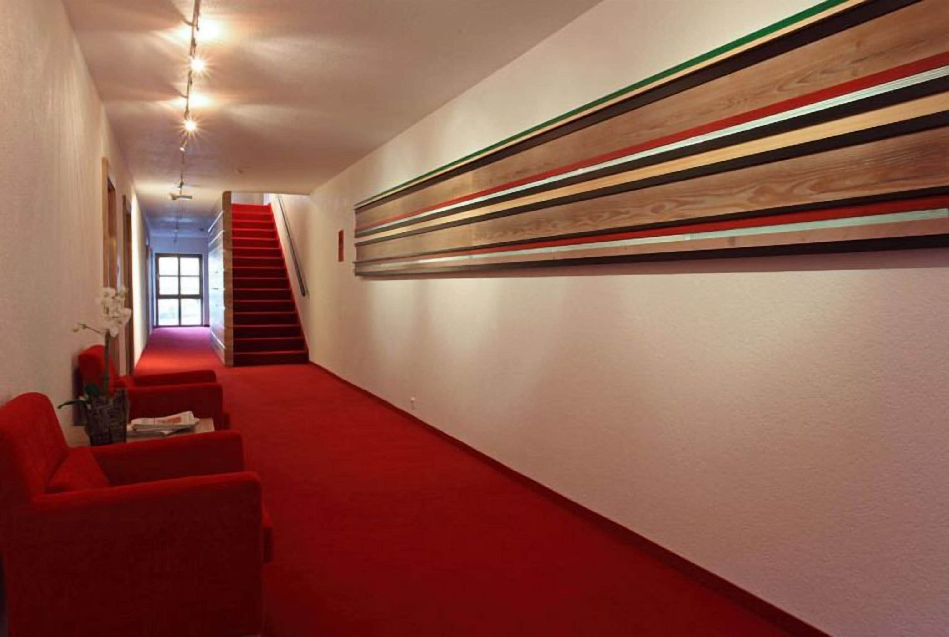 A hallway with red carpet, a staircase, and a wall with horizontal wooden panels.