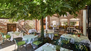 An outdoor dining area with tables and chairs, surrounded by greenery and stone walls. - Hotel Restaurant Adler (Lahr)