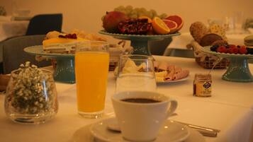 Una mesa de desayuno con cruasanes, fruta, un vaso de jugo de naranja, una taza de café y un frasco pequeño de mermelada.