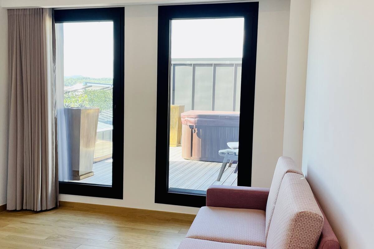 A modern living room with a large window, a sofa, and a wooden floor.