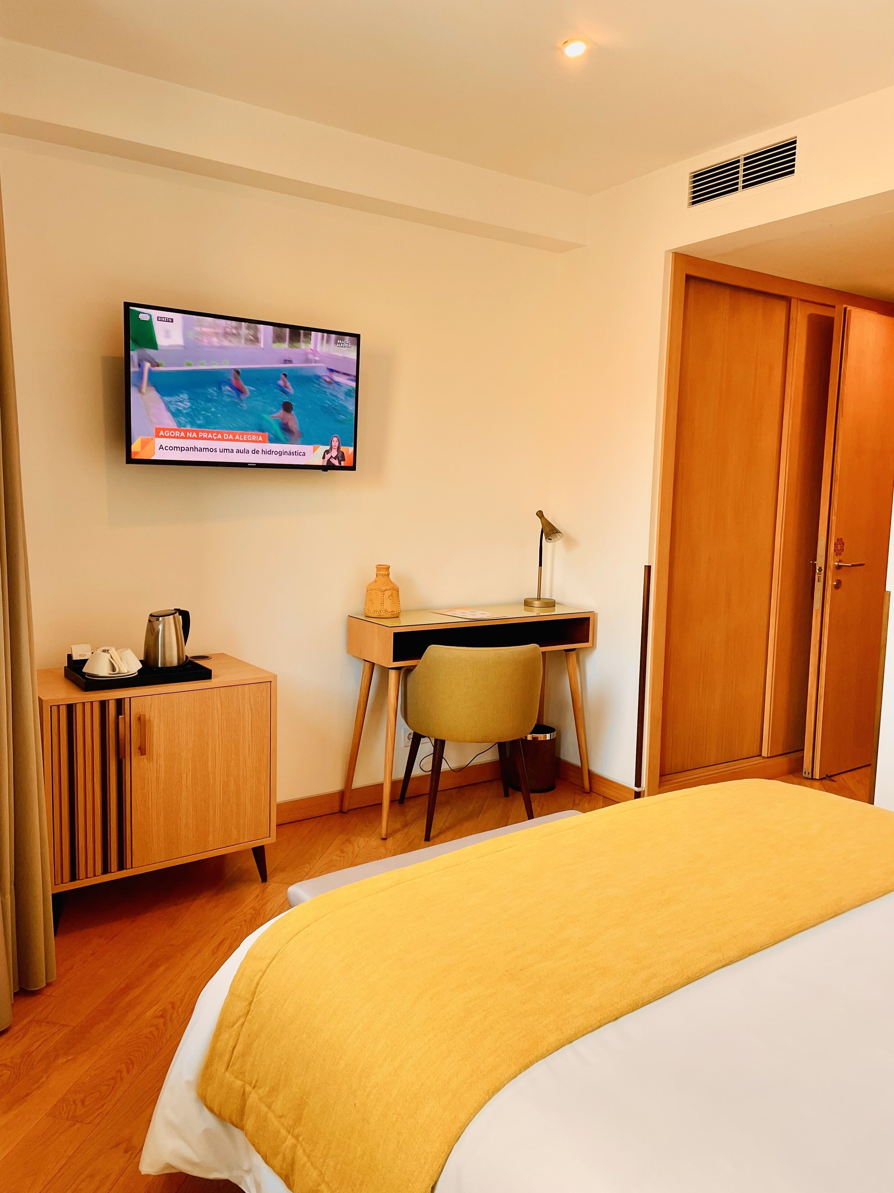 A hotel room with a bed, a desk with a chair, a television, and a wardrobe.