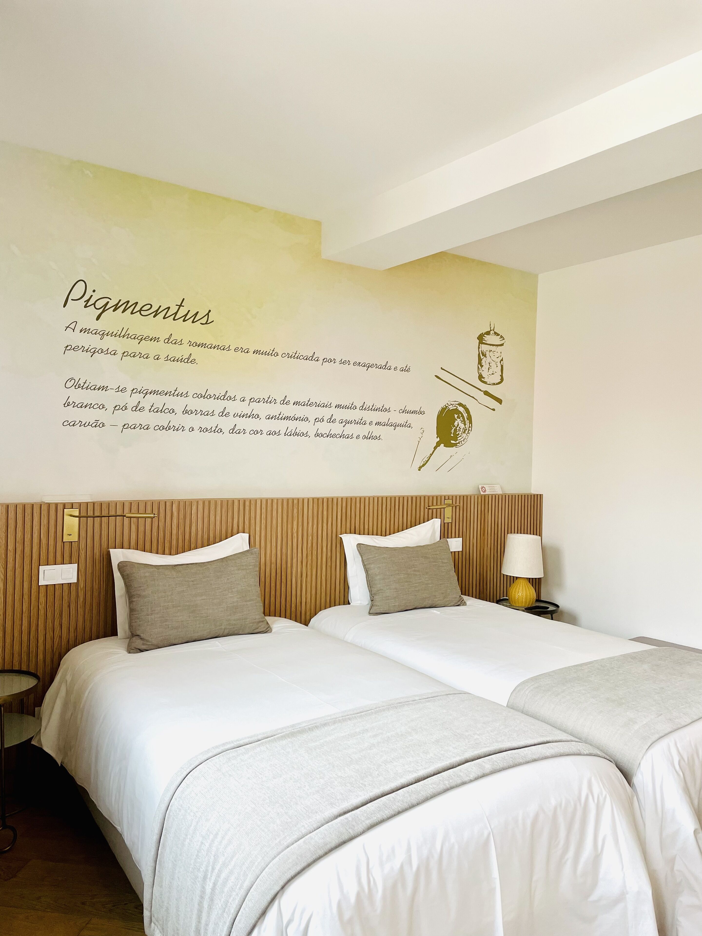 A hotel room with two beds, a wooden headboard, a nightstand with a lamp, and a wall with text and illustrations.
