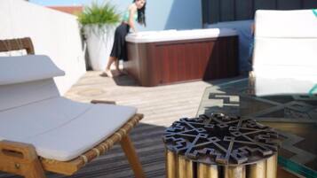 Una terraza de madera con una silla lounge blanca, una mesa de vidrio y un adorno metálico.