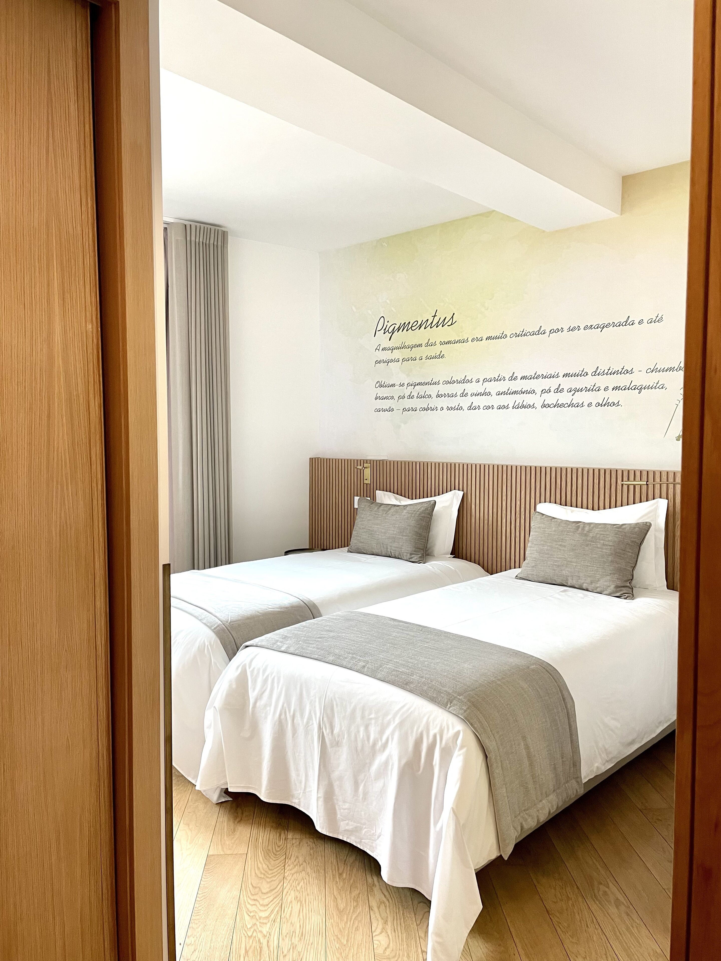 A hotel room with two beds, wooden headboards, a wall with a text poster, and a wooden floor.