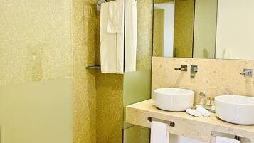 Un baño moderno con ducha de vidrio, dos lavamanos y un espejo grande.
