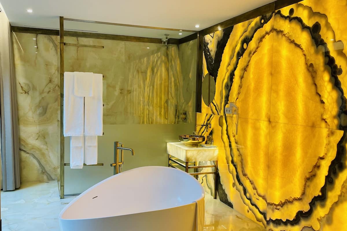 A modern bathroom with a freestanding bathtub, marble flooring, and a large decorative wall piece.