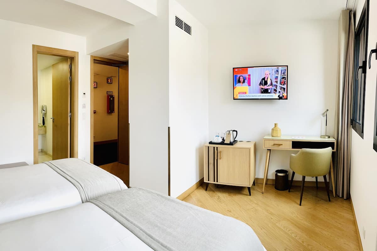A hotel room with a bed, a desk, a chair, a TV, and a small cabinet.