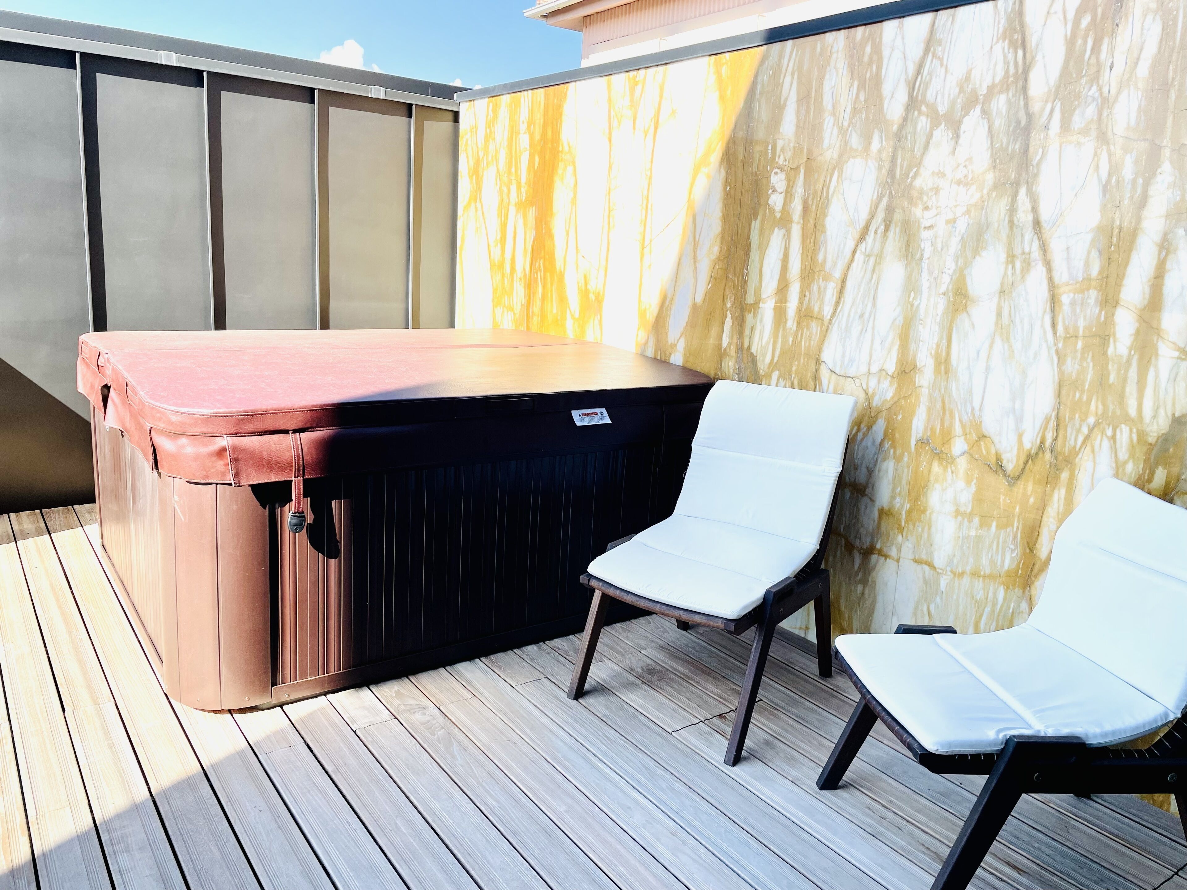 A hot tub with a wooden deck and a white lounge chair.
