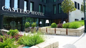 The exterior of the Castello Hotel with a modern facade, large windows, and a landscaped garden area with various plants and a pathway leading to the entrance. - Castelo Hotel (Chaves)