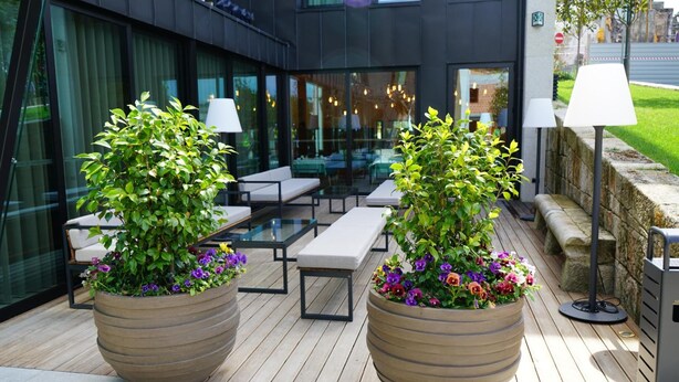 An outdoor seating area with two large planters of flowers, a glass table, and benches. - Castelo Hotel (Chaves)