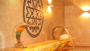 A spa room with a marble pool, a wall-mounted circular design, and two curved benches. - Castelo Hotel (Chaves)