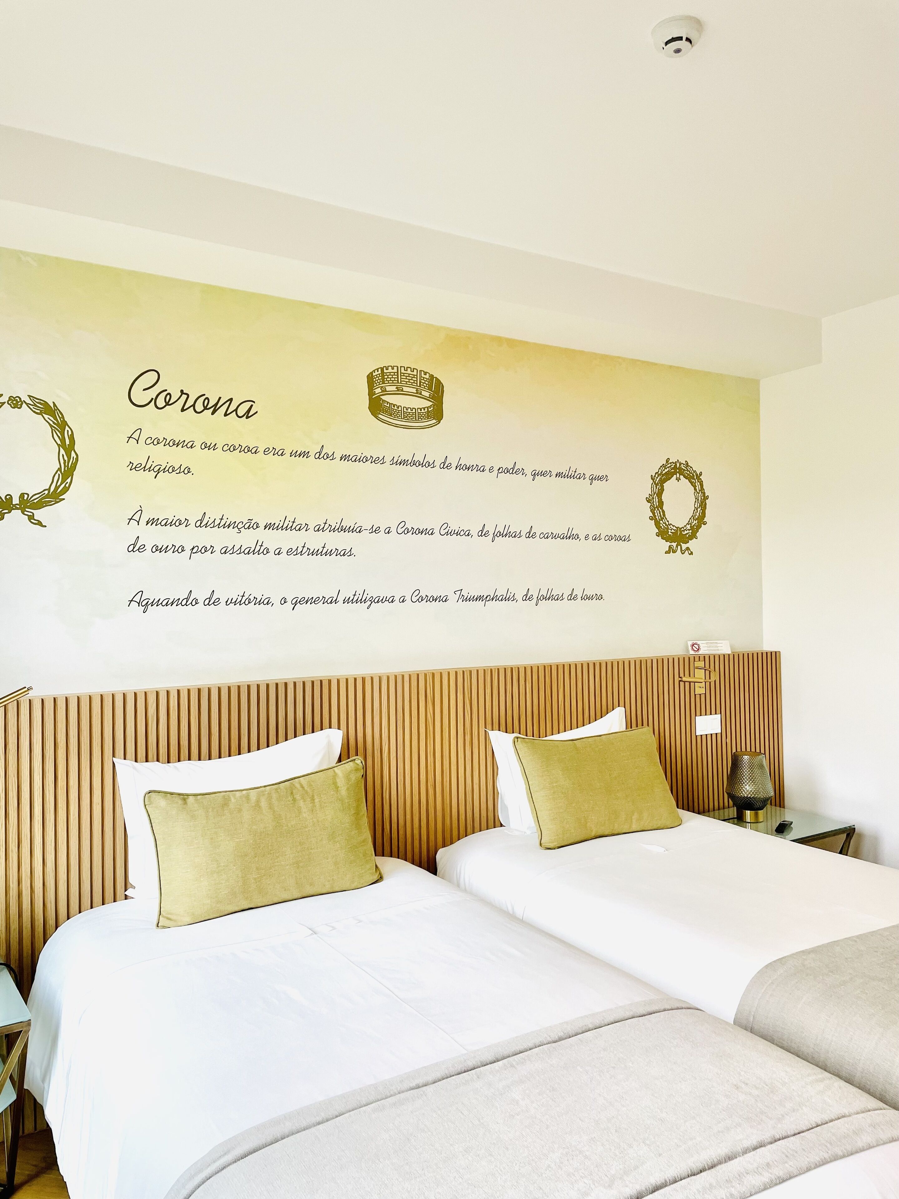 Ein Hotelzimmer mit zwei Betten, einem Holzkopfende und einer Wand mit Schriftzügen und Kronensymbolen.