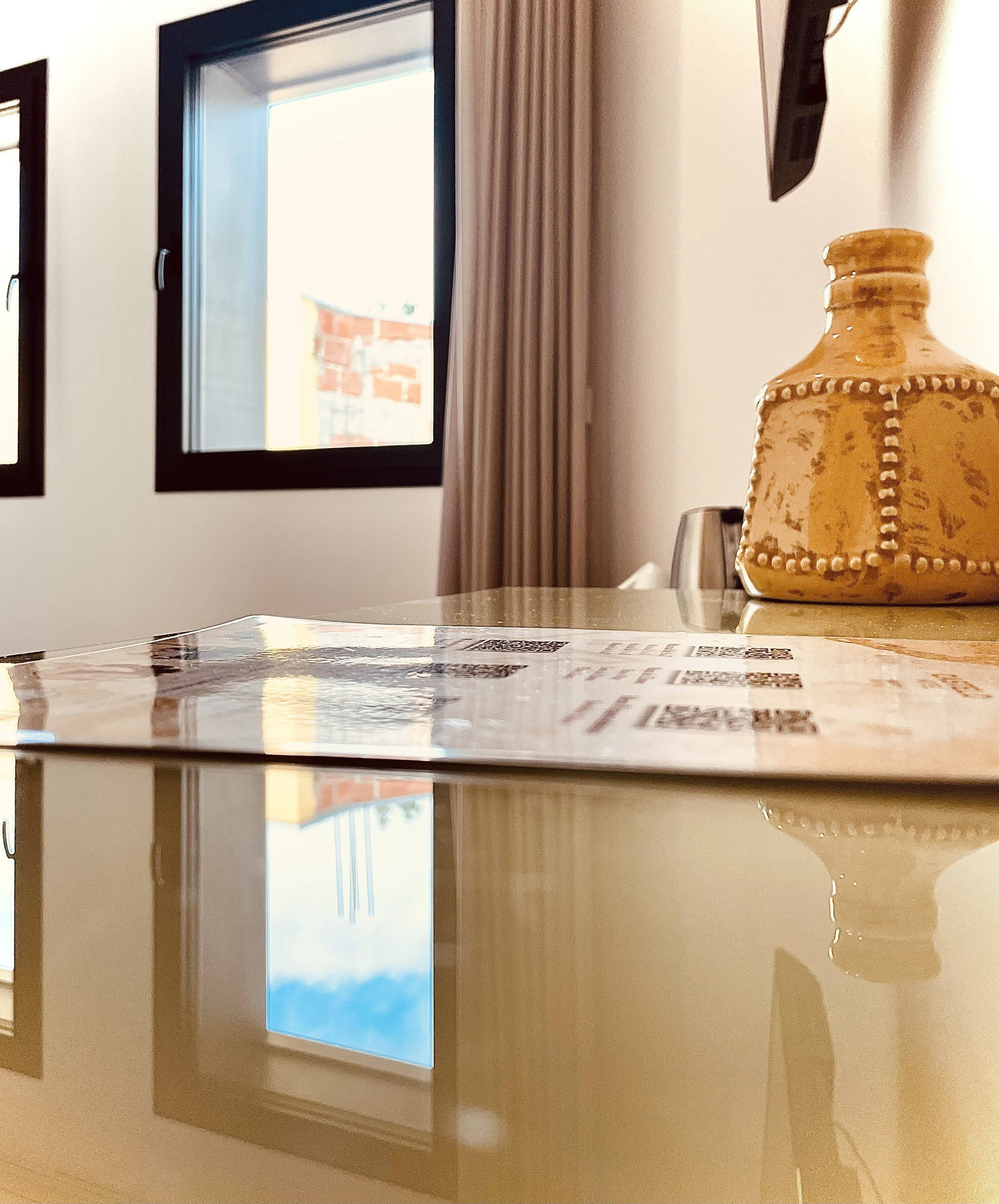 A table with a newspaper, a decorative vase, and a window with curtains.