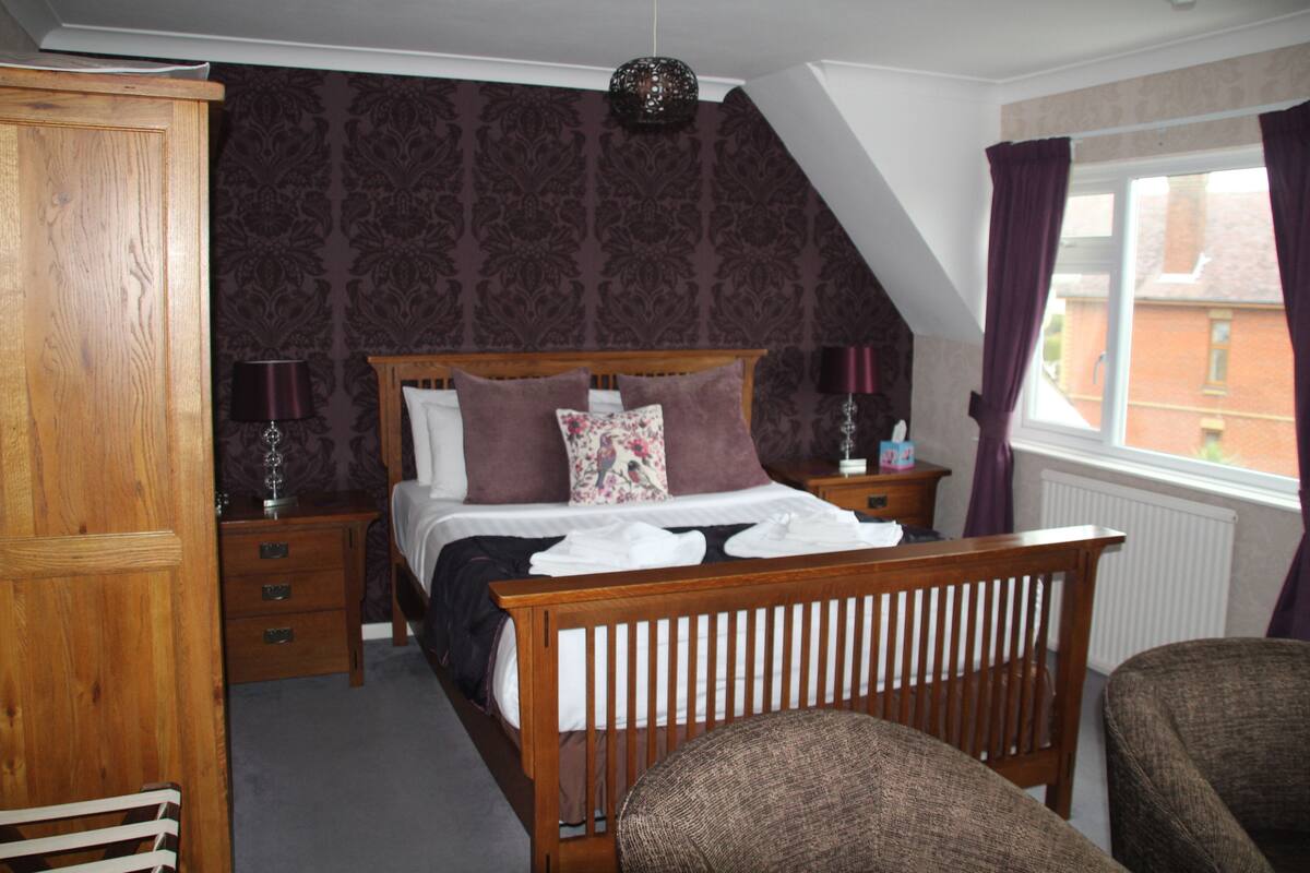 A bedroom with a wooden bed, a nightstand, a dresser, and a window with curtains.
