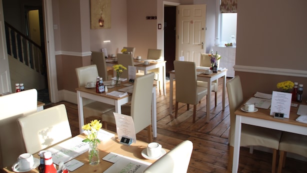 A hotel dining area with multiple tables, chairs, and a staircase. - The Kenbury (Shanklin)