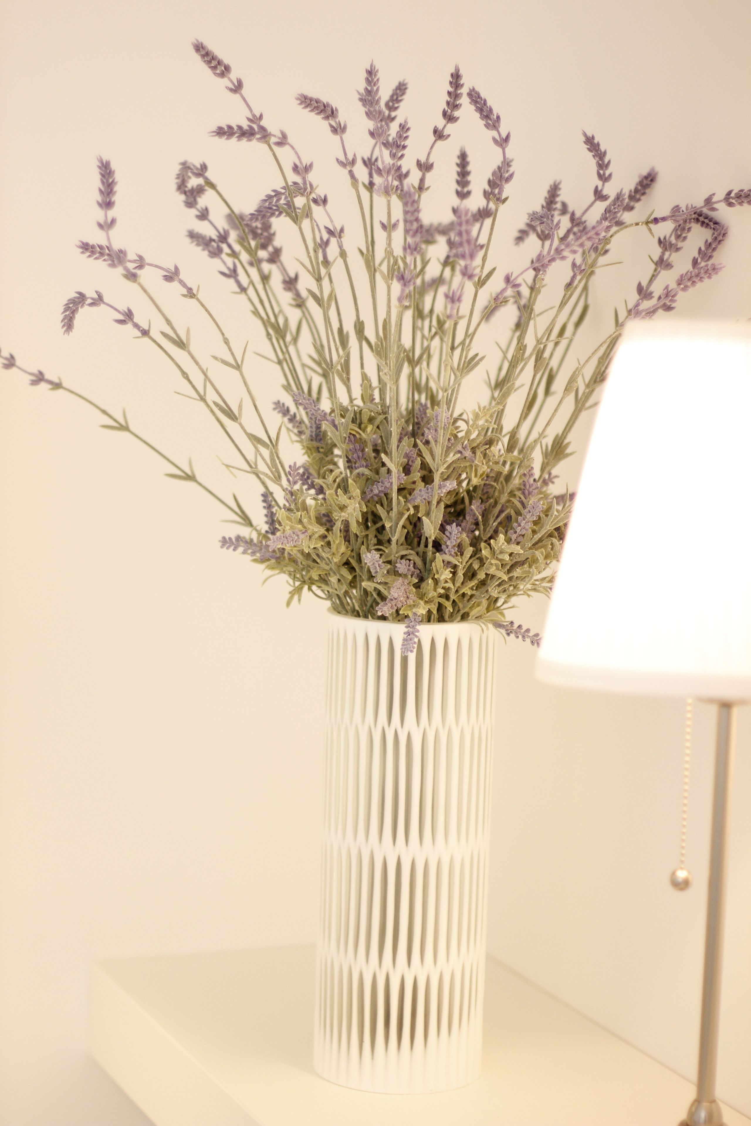A white vase with a textured pattern containing lavender flowers.