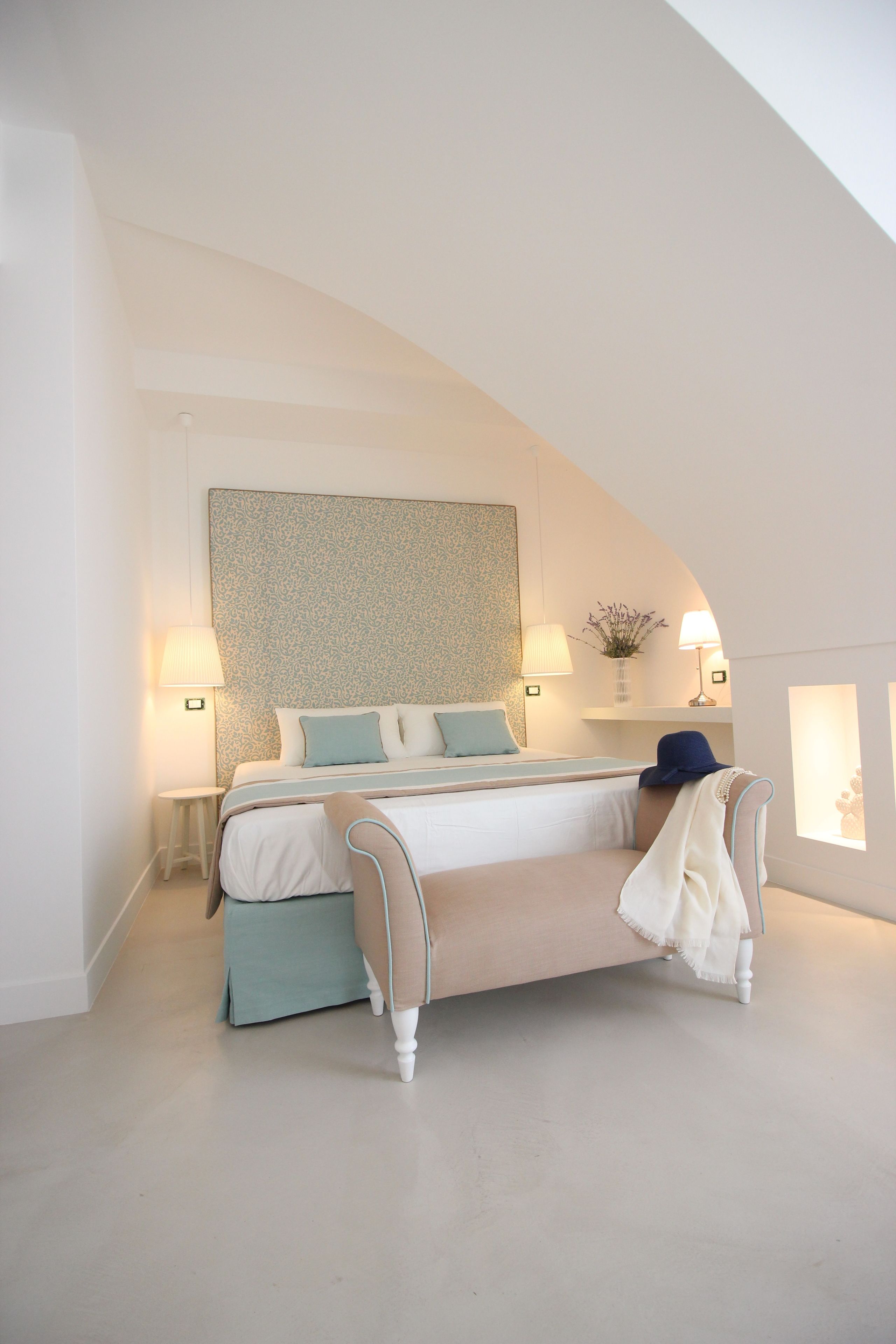 Un dormitorio con cama, lámparas de noche, mesita de noche y un jarrón decorativo.