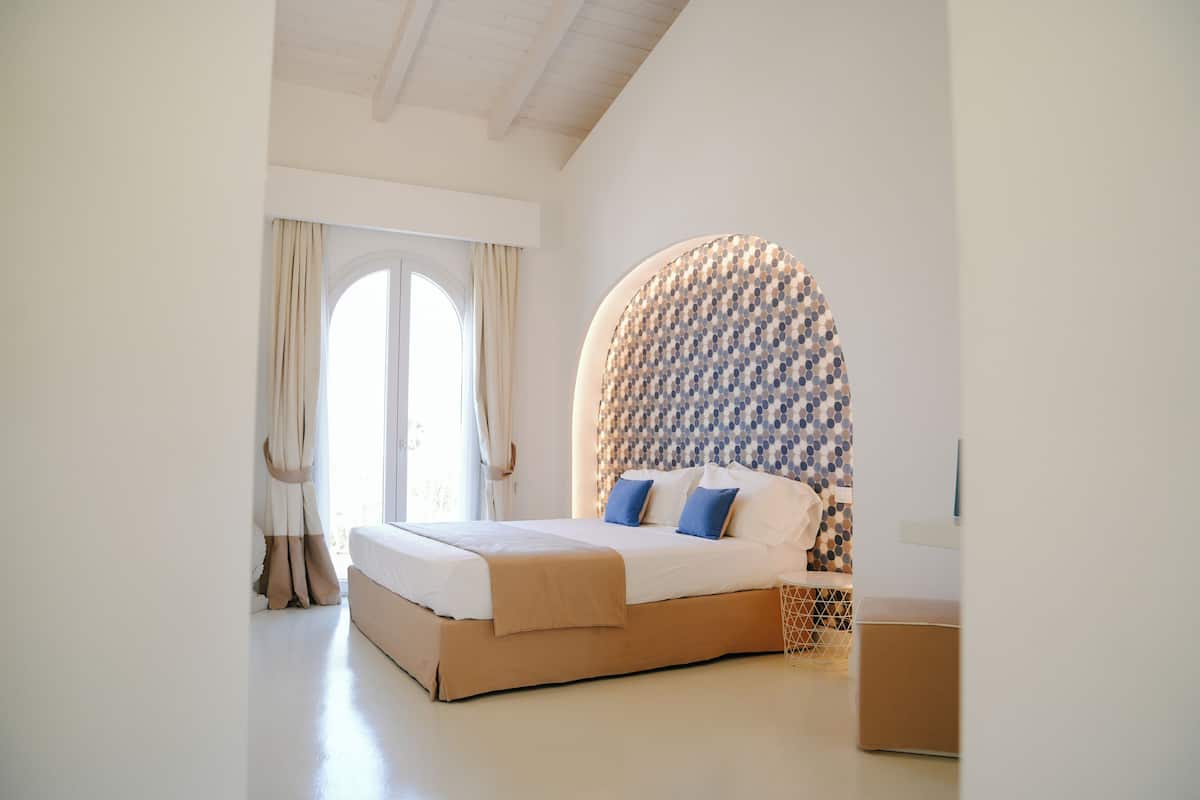 A bedroom with a bed, a window with curtains, and a patterned wall.